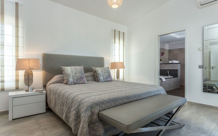 Modern bedroom featuring a gray bed with a large window, white and gray decor, and a minimalist style.