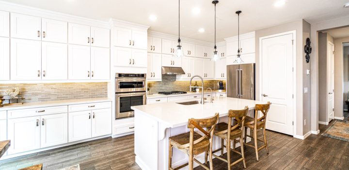 Bright kitchen space with white cabinetry, a large central island with seating, and contemporary lighting, creating a clean and inviting cooking environment.