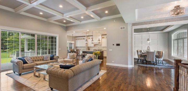 Spacious open plan living area with a luxurious tufted sofa set, modern kitchen in the background, and a dining area, all under a striking coffered ceiling.