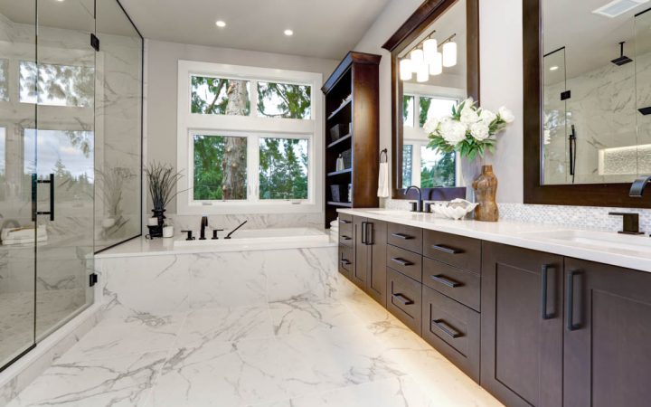 Luxuriously appointed bathroom with marble details, a freestanding bathtub, and a view of the forest through large windows.