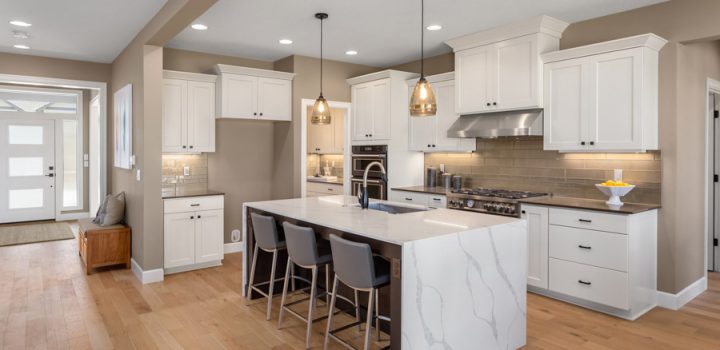 Sleek and sophisticated kitchen design showcasing white cabinetry, marble island, and pendant lighting over a hardwood floor.