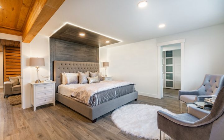 Spacious bedroom featuring a large bed with gray upholstered headboard, wooden ceiling details, and modern furnishings.